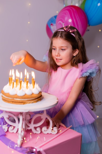 Bambina carina in un bel vestito esprime un desiderio e spegne le candeline sulla torta di compleanno