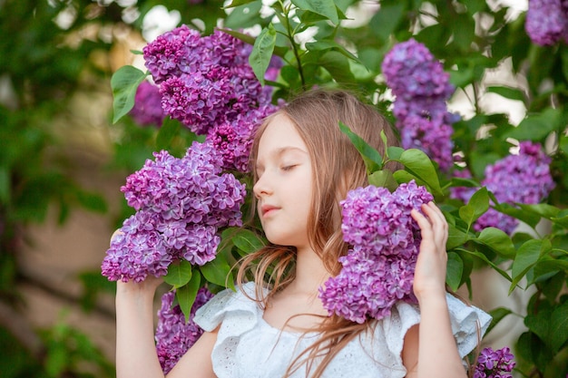 Bambina carina in un lillà in fiore in primavera