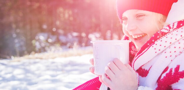 Bambina carina in vestiti caldi e con una tazza di cioccolata calda in una giornata nevosa