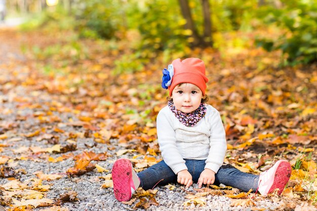 Bambina carina seduta in un mucchio di foglie gialle.