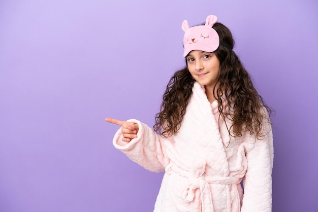 Bambina caucasica in pigiama isolata su sfondo viola sorpresa e puntando il dito di lato