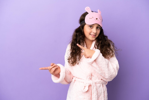 Bambina caucasica in pigiama isolato su sfondo viola sorpreso e rivolto verso il lato