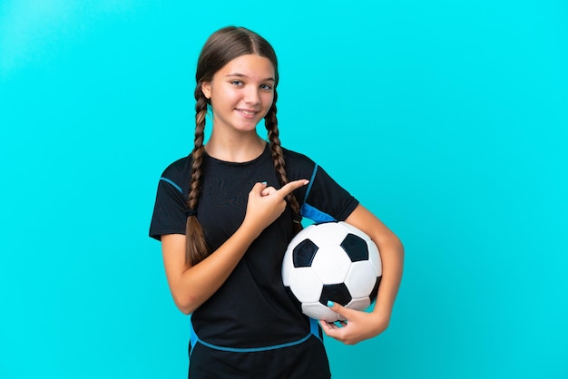 Bambina caucasica isolata su sfondo blu con pallone da calcio e rivolta verso il lato