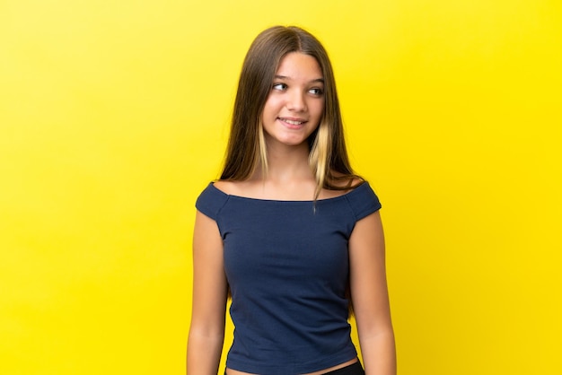 Bambina caucasica isolata su sfondo giallo che guarda al lato e sorridente