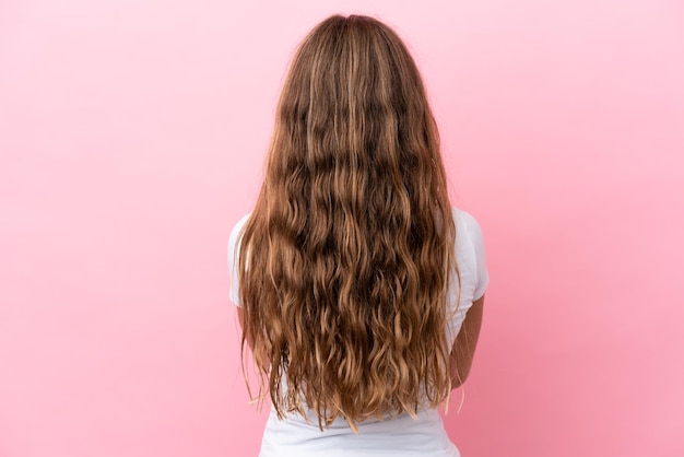 Bambina caucasica isolata su sfondo rosa in posizione posteriore