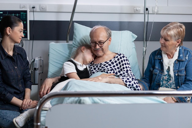 Bambina che abbraccia il nonno nella stanza del sanatorio prima dell'intervento chirurgico nella torre medica. Un vecchio ricoverato saluta i familiari più stretti nell'ospedale per anziani.
