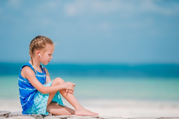 Bambina che ascolta la musica sulle cuffie sulla spiaggia caraibica