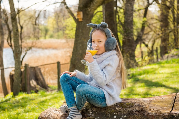 Bambina che beve il succo di vitamina arancione al mattino nel parco all'aperto in primavera.