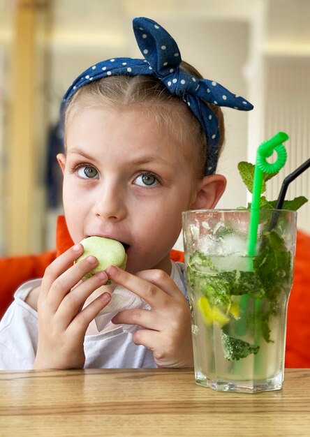 Bambina che beve mojito analcolico e mangia amaretti in un caffè