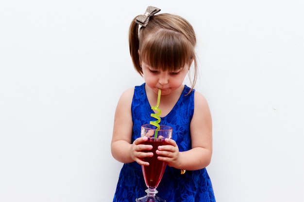 Bambina che beve rinfresco all'uva spina con paglia divertente, sfondo bianco