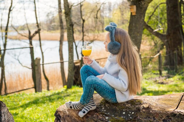 Bambina che beve succo di vitamina arancione al mattino nel parco all'aperto in primavera