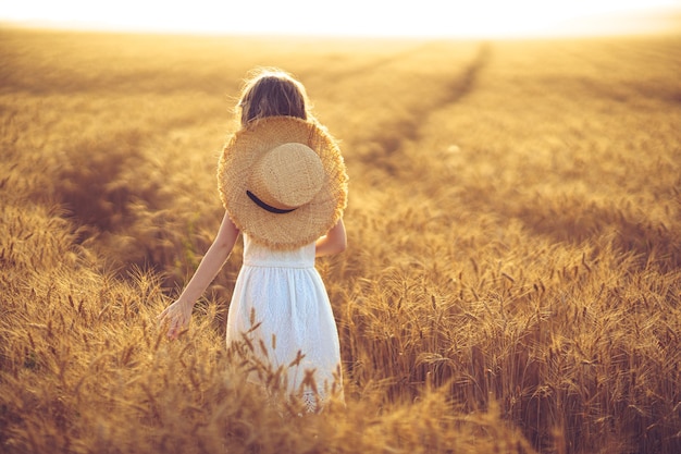 Bambina che cammina nel campo di grano al tramonto