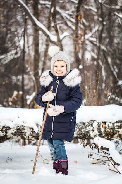 Bambina che cammina nella foresta invernale in una giacca blu e un cappello grigio