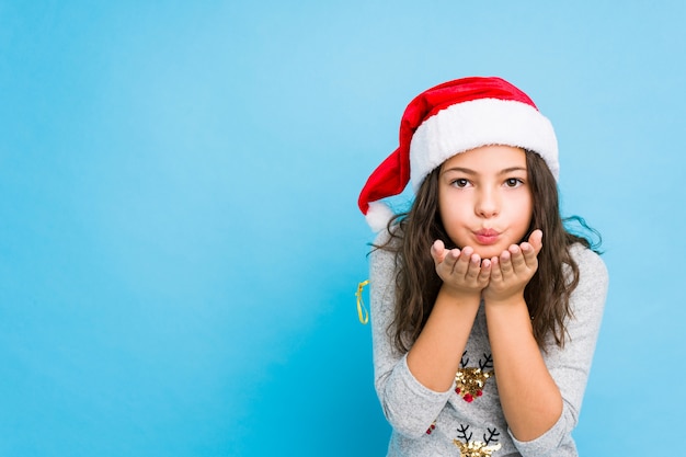 Bambina che celebra il giorno di Natale piegando le labbra e tenendo le palme per inviare bacio dell'aria.