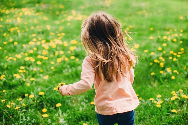 Bambina che corre lungo il prato verde con denti di leone gialli