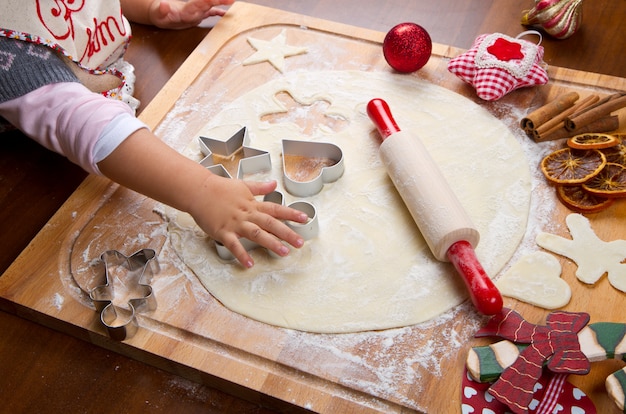 Bambina che cuoce i biscotti di Natale che tagliano pasticceria con un cooki