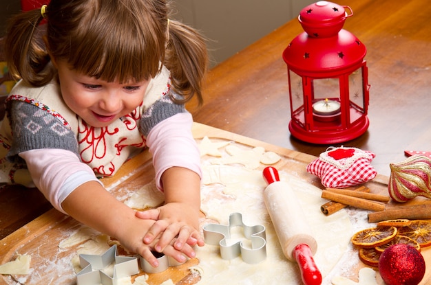 Bambina che cuoce i biscotti di Natale che tagliano pasticceria con un cooki