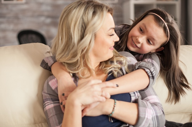 Bambina che dà affetto a sua madre mentre la abbraccia da dietro. Figlia con bretelle.