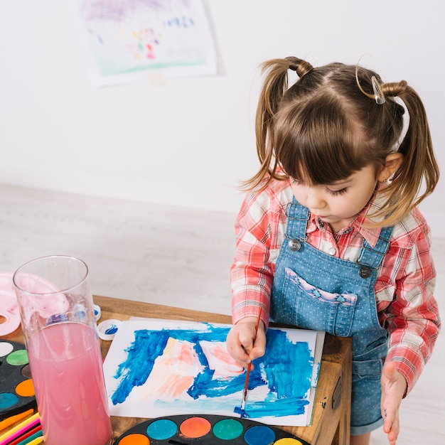 Bambina che dipinge con l&#39;aquarelle al tavolo di legno