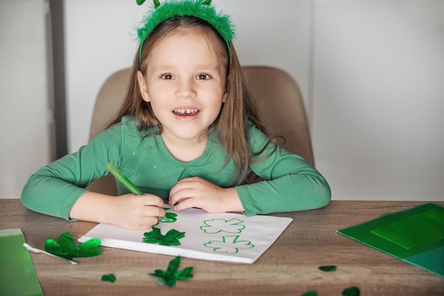 Bambina che dipinge e taglia quadrifogli verdi per il giorno di San Patrizio al tavolo