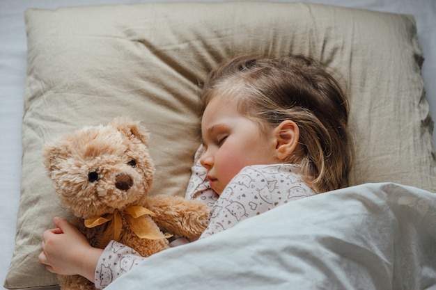 Bambina che dorme nel letto abbracciando il peluche a casa, vista dall'alto