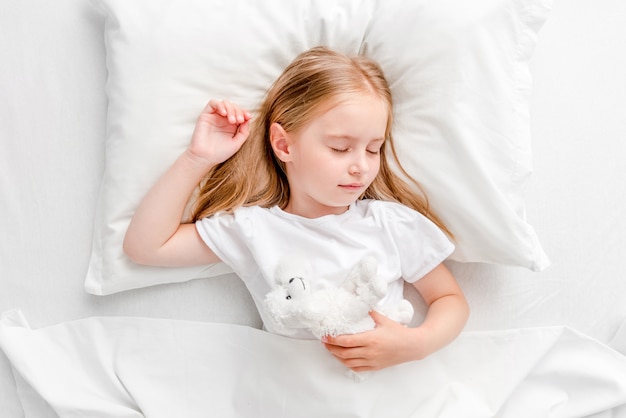 Bambina che dorme nel letto bianco