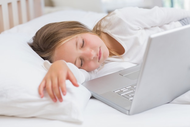 Bambina che dorme nel suo letto davanti al computer portatile