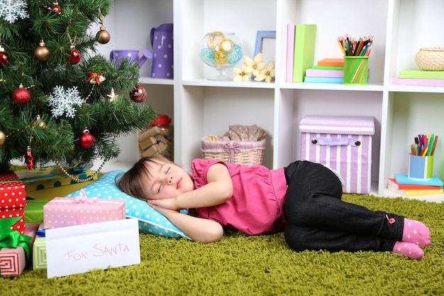 Bambina che dorme vicino all'albero di Natale in camera