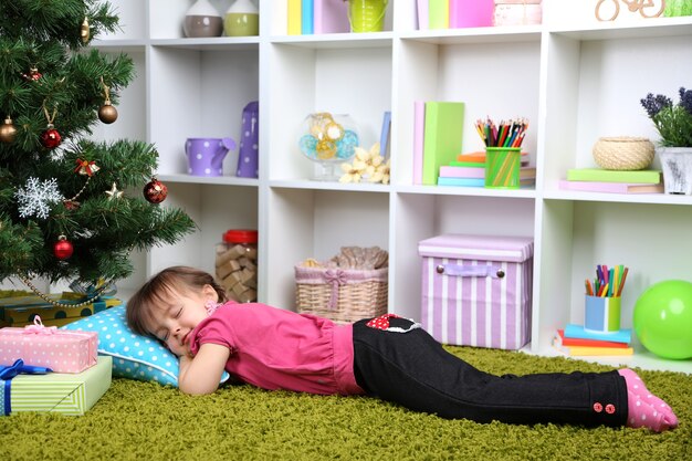 Bambina che dorme vicino all'albero di Natale in camera