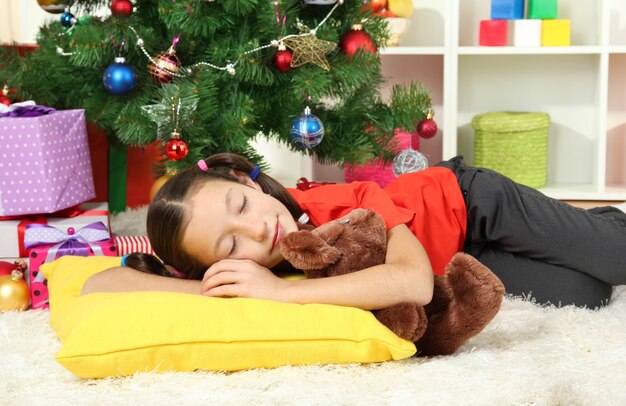 Bambina che dorme vicino all'albero di Natale