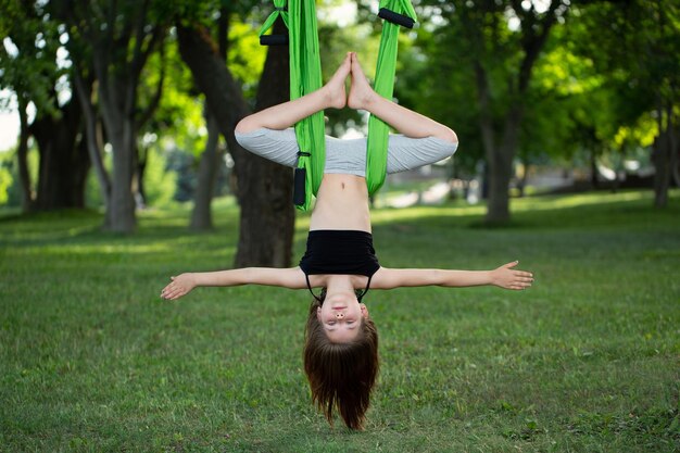 Bambina che fa esercizi di yoga con un'amaca nel parco