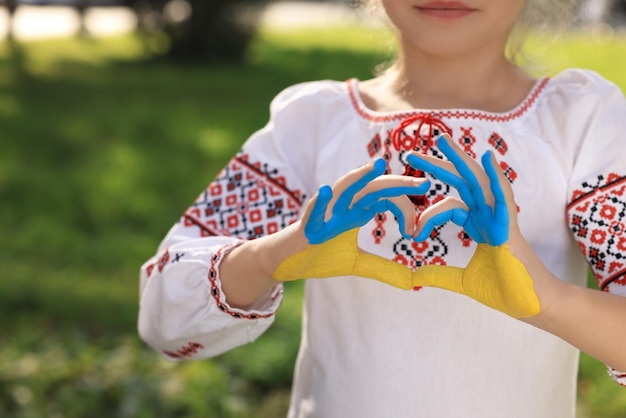 Bambina che fa il cuore con le mani dipinte nei colori della bandiera ucraina all'aperto primo piano e spazio per il testo Concetto di amore Ucraina