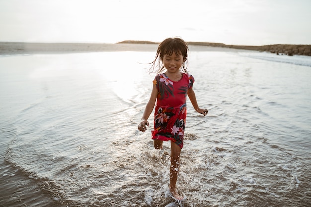 Bambina che funziona sulla spiaggia mentre gioca con acqua