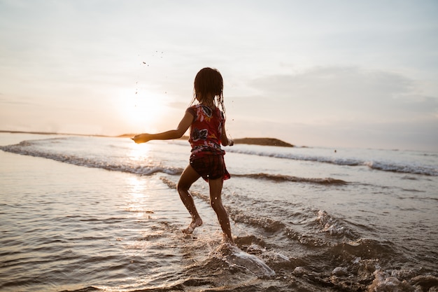 Bambina che funziona sulla spiaggia mentre gioca con acqua