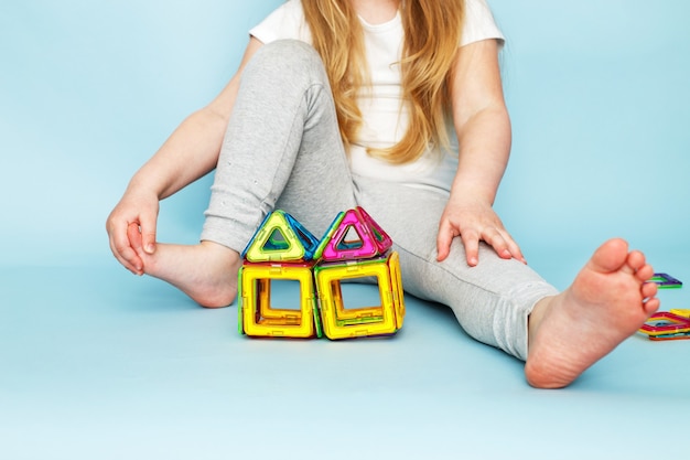 Bambina che gioca con il giocattolo costruttore magnetico colorato su sfondo blu. bambino ha costruito una casa
