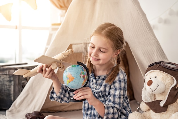 Bambina che gioca con il globo e l'aereo di legno che si siede vicino al wigwam nella stanza dei bambini