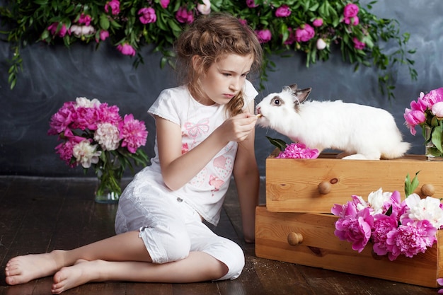 Bambina che gioca con il vero coniglio. Bambino e coniglietto bianco a Pasqua. Bambino bambino alimentazione animale da compagnia. I bambini e gli animali domestici giocano. Divertimento e amicizia per animali e bambini.