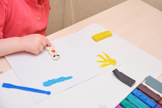 Bambina che gioca con la plastilina colorata sul tavolo. Gioco di educazione domestica con l'argilla. Concetto di sviluppo iniziale che il bambino scolpisce dalla plastilina