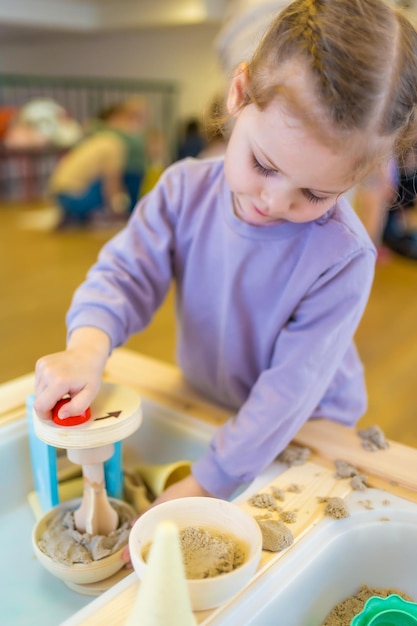 Bambina che gioca con la sabbia cinetica e lo sviluppo sensoriale dei giocattoli di legno e sperimenta l'atto a tema