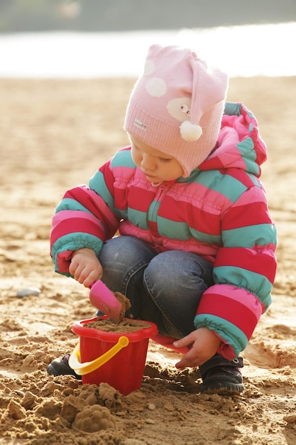 Bambina che gioca con la sabbia in spiaggia d'autunno