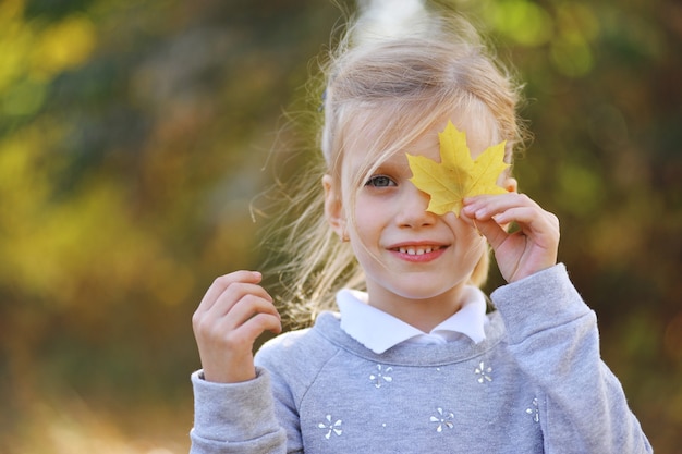 Bambina che gioca con le foglie gialle nella sosta di autunno