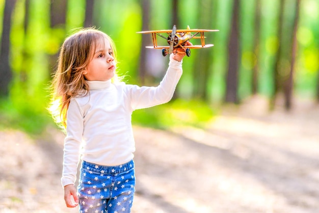 Bambina che gioca con un aeroplano giallo nella foresta