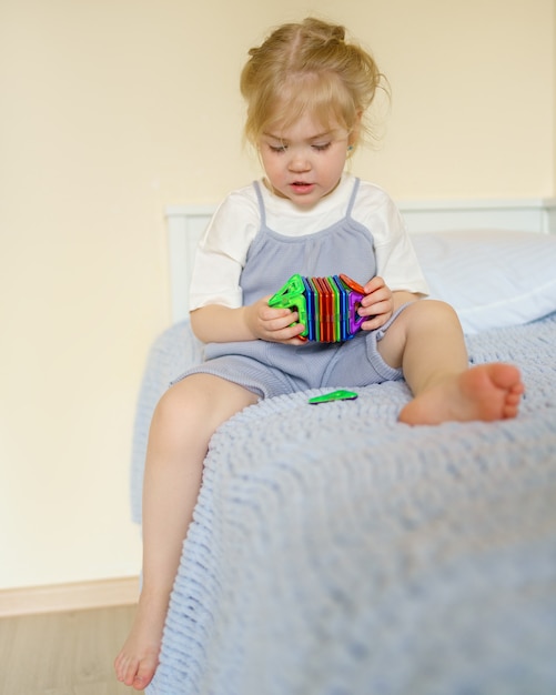 Bambina che gioca con un giocattolo magnetico mentre è seduta sul letto