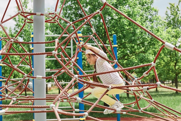 Bambina che gioca e si diverte arrampicandosi giocando con le corde giochi estivi per bambini e divertimento all'aperto attività di svago nel campo indossando abbigliamento casual