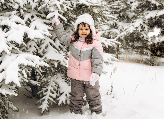 Bambina che gioca in inverno nella foresta innevata. Bellissimo ritratto del bambino d'inverno. Bambino felice, divertimento invernale all'aperto.
