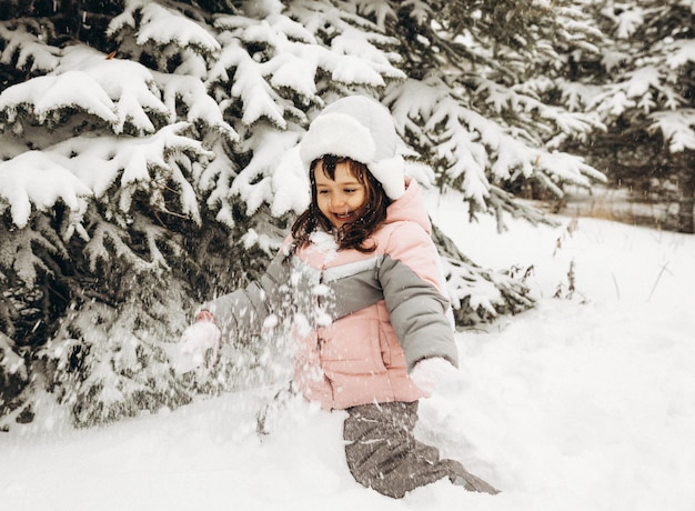 Bambina che gioca in inverno nella foresta innevata. Bellissimo ritratto del bambino d'inverno. Bambino felice, divertimento invernale all'aperto.