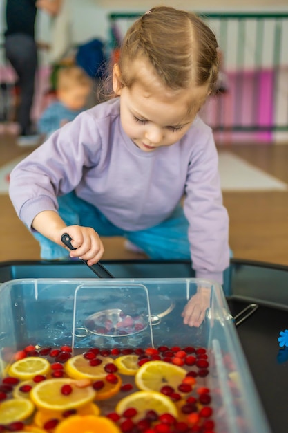 Bambina che gioca in una barra di frutta fatta a mano con bacche da cucina e sviluppo sensoriale di agrumi