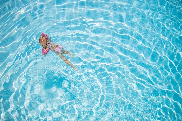 Bambina che gioca nell'acqua della piscina all'aperto durante le vacanze estive Bambino che impara a nuotare