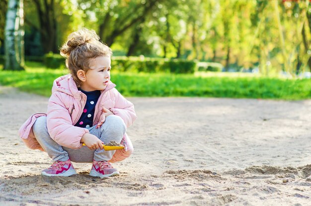 Bambina che gioca nella sabbia nel parco in una giornata autunnale.