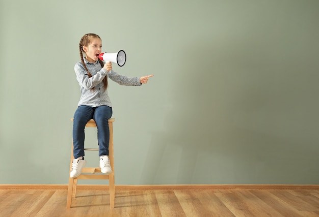 Bambina che grida nel megafono mentre era seduto su una sedia contro il muro di colore